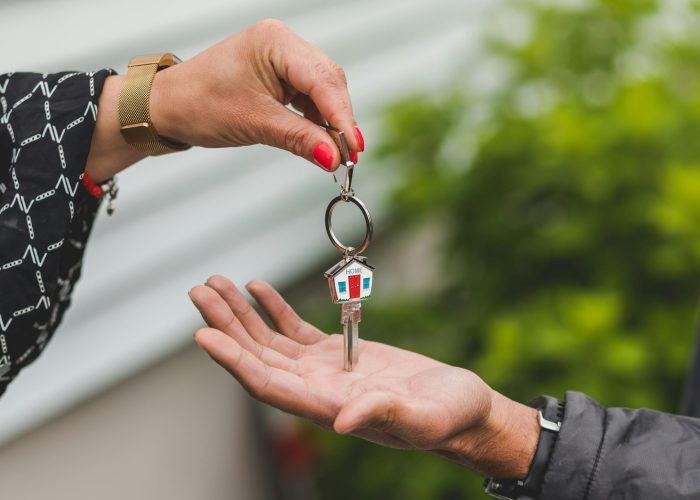 Close-up of a hand handing over a key with a house keychain, symbolizing real estate transaction.